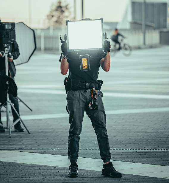 A person in dark clothing holds a bright, rectangular light source up outdoors, obscuring their face.