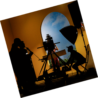 Silhouetted film crew and equipment against a vibrant yellow backdrop with a blue sky visible through an arched window